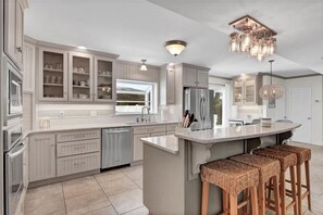 Una cocina moderna con armarios blancos, una isla central, taburetes de bar y una araña.