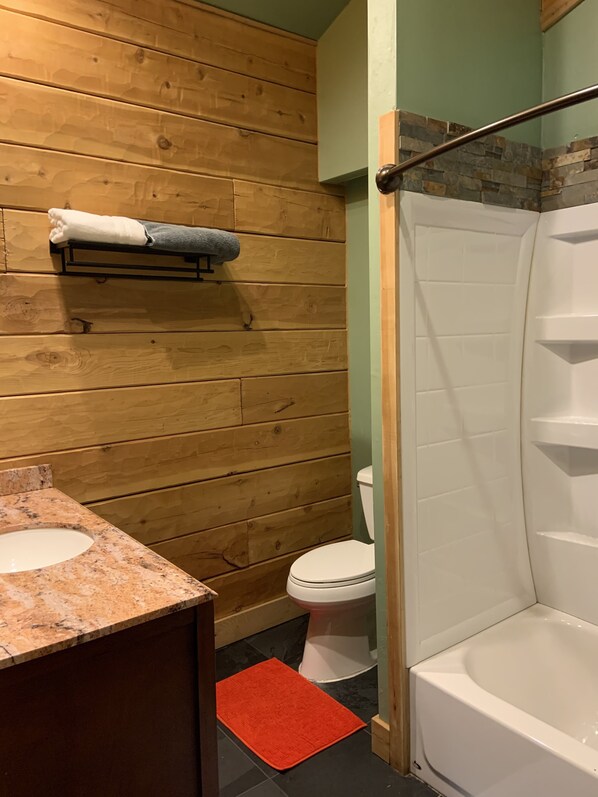 Een badkamer met houten wanden, een wit toilet, een bad en een granieten aanrecht.
