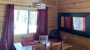 Interior de una cabaña de madera con una mesa de comedor, sillas y una lámpara colgante.