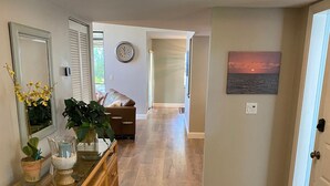 Un couloir doté d’un plancher en bois, une console en osier agrémentée d’objets décoratifs, un canapé et un tableau accroché au mur.