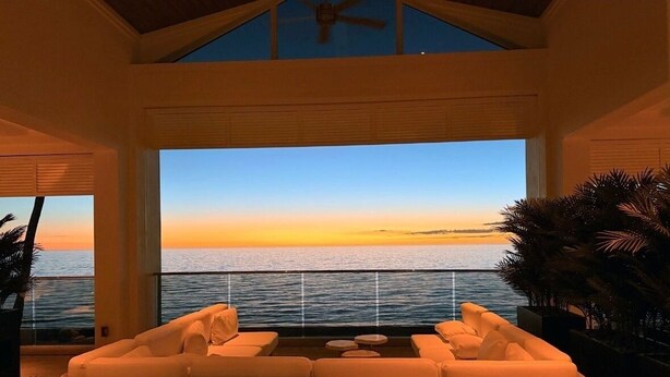 Un balcon avec des meubles en osier, une vue sur la mer et un ventilateur de plafond.
