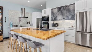 A modern kitchen with a central island, bar stools, stainless steel appliances, and a marble backsplash. - Private & Spacious [2300sqft] home w/Pool,Hot Tub,Golf Cart, Pet Friendly & Club (Captiva)