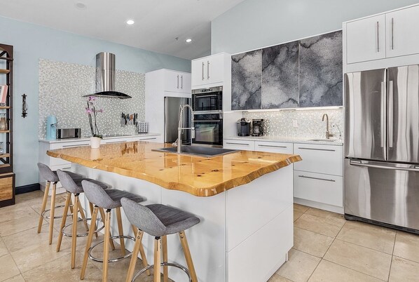 A modern kitchen with a central island, bar stools, stainless steel appliances, and a marble backsplash. - Private & Spacious [2300sqft] home w/Pool,Hot Tub,Golf Cart, Pet Friendly & Club (Captiva)