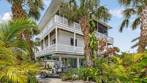 A two-story house with a balcony, surrounded by tropical vegetation. - Private & Spacious [2300sqft] home w/Pool,Hot Tub,Golf Cart, Pet Friendly & Club (Captiva)