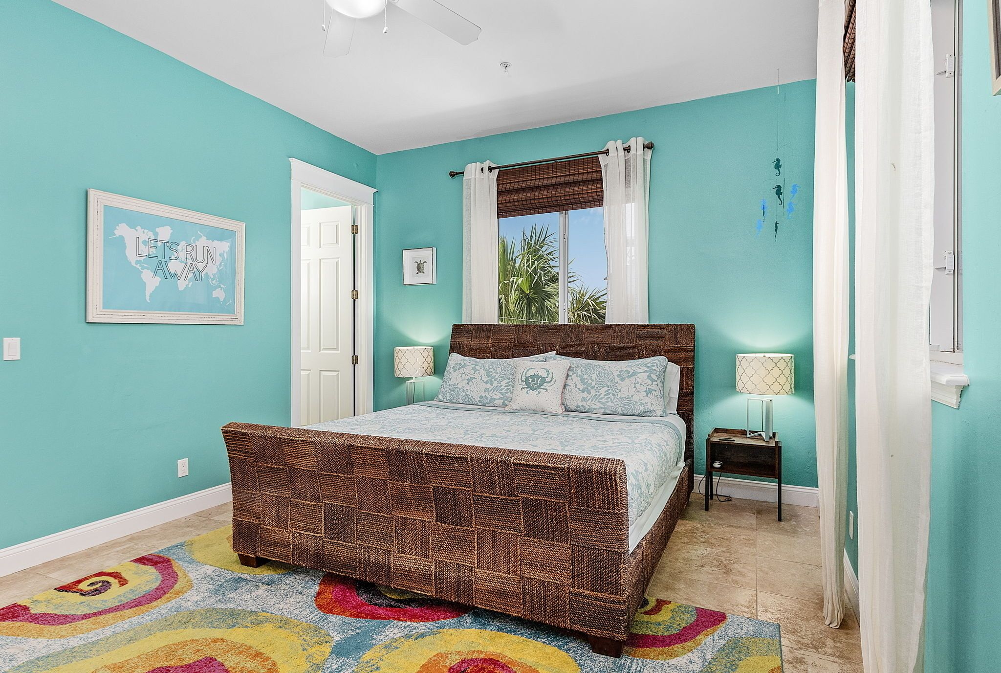 A bedroom with a bed, a window with curtains, a wall with a picture, and a door.