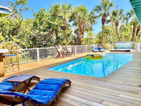 A wooden deck with a pool, lounge chairs, and a floating ring.