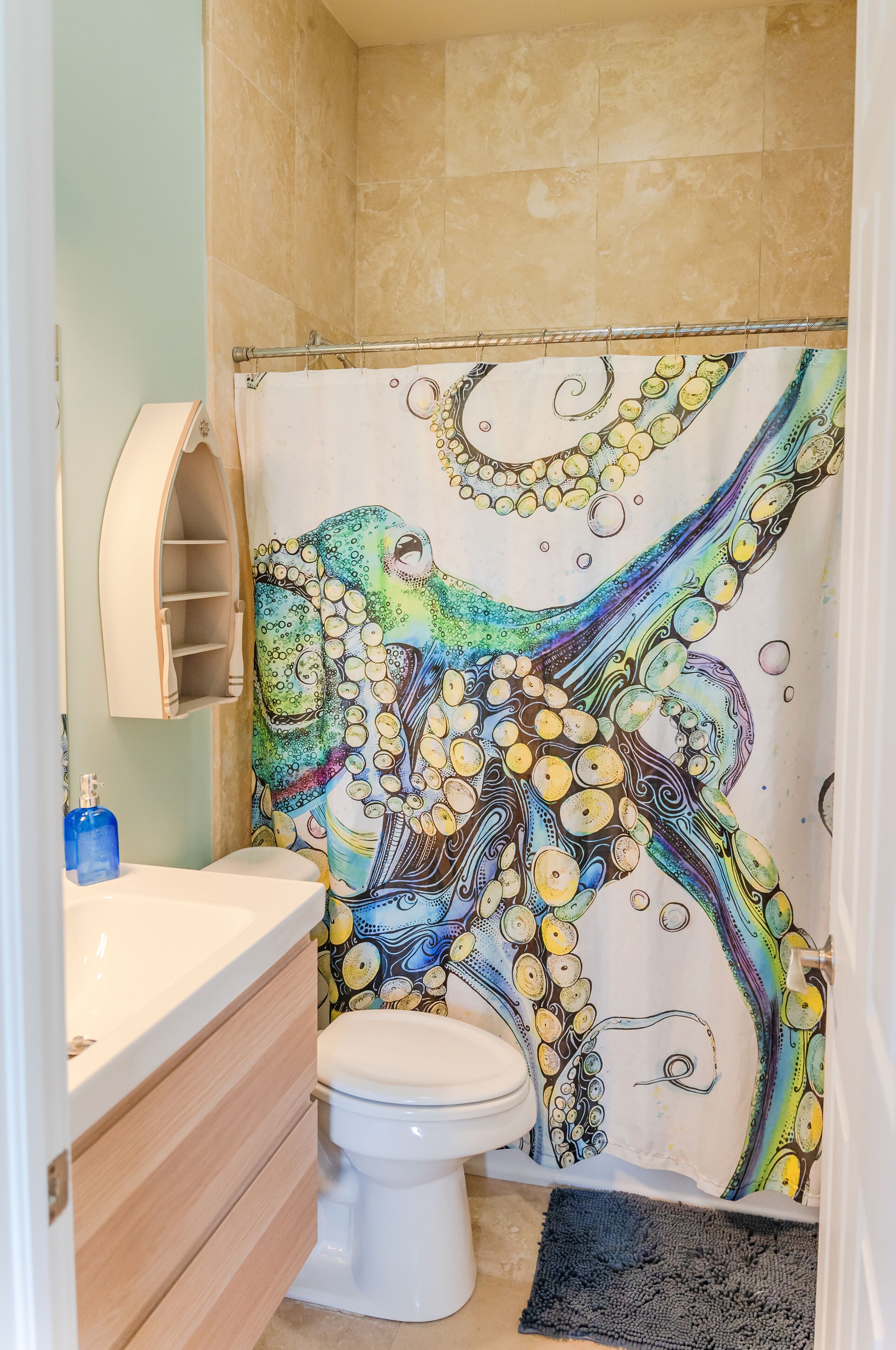 Une salle de bain avec des toilettes blanches, un lavabo beige et un rideau de douche orné d’un motif de poulpe.