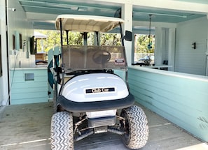 Golf cart parked under a covered porch with a wooden deck.