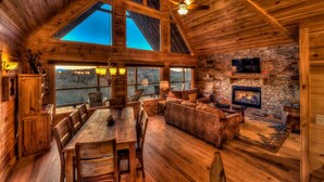A spacious wooden cabin with a dining area, seating, and a stone fireplace. - Alpine Ridge - Mountain Views | Close to Down Town Blue Ridge | Hot Tub | Shuffleboard (Blue Ridge)