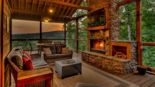 A cozy outdoor seating area with a stone fireplace, wicker furniture, and a view of the surrounding landscape. - Alpine Ridge - Mountain Views | Close to Down Town Blue Ridge | Hot Tub | Shuffleboard (Blue Ridge)