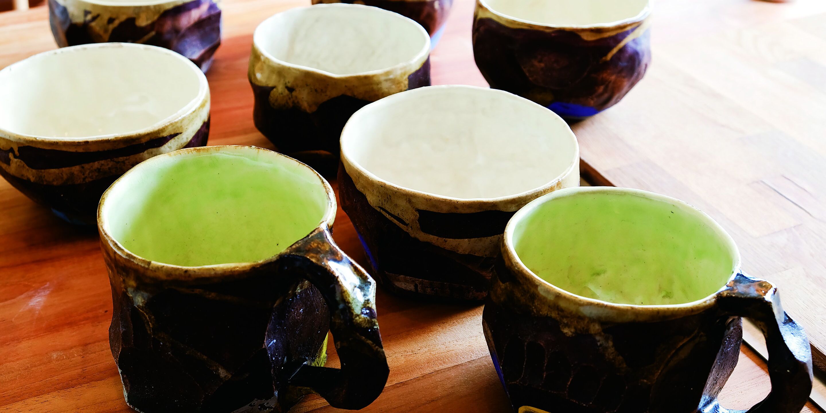 A collection of ceramic mugs with handles, some with green interiors, arranged on a wooden surface.