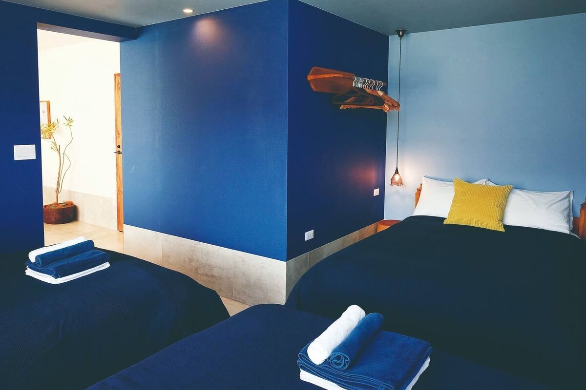 Quarto de hotel com duas camas, uma mesa de cabeceira, uma luminária e um vaso com planta.