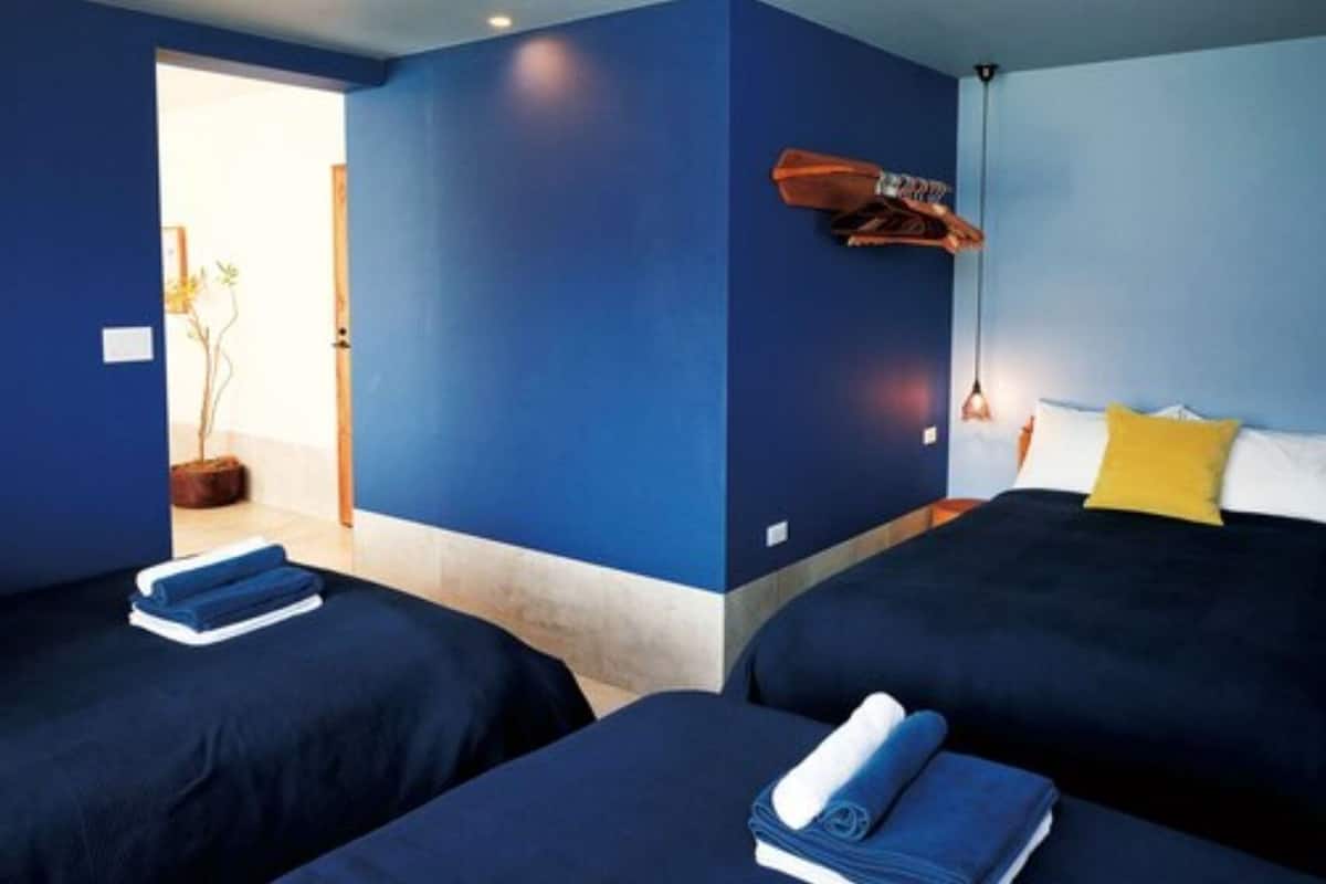 Quarto com duas camas, cabeceira de madeira, luminária pendente e uma pequena mesa com uma cadeira.
