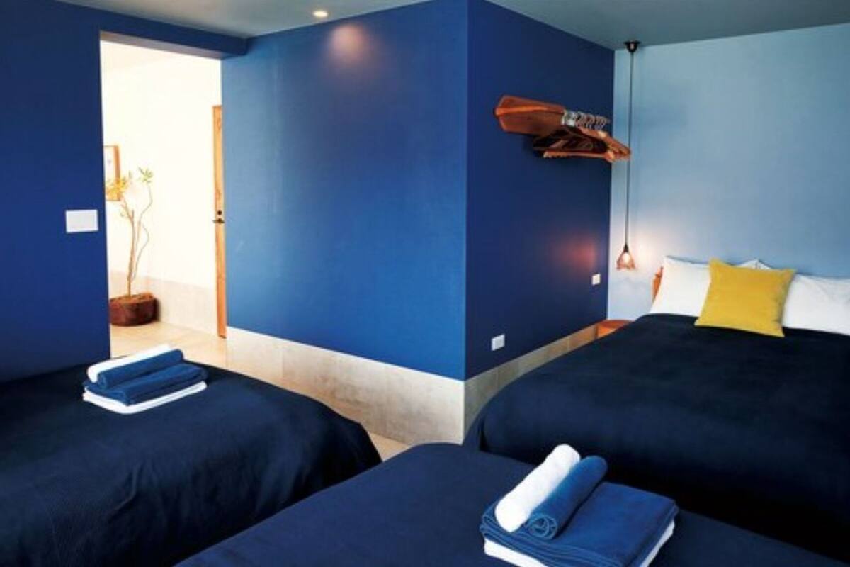 Quarto com duas camas, cabeceira de madeira, luminária pendente e uma pequena mesa com uma cadeira.