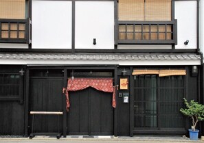 A traditional Japanese building with black sliding doors, a tiled roof, and a small potted plant.