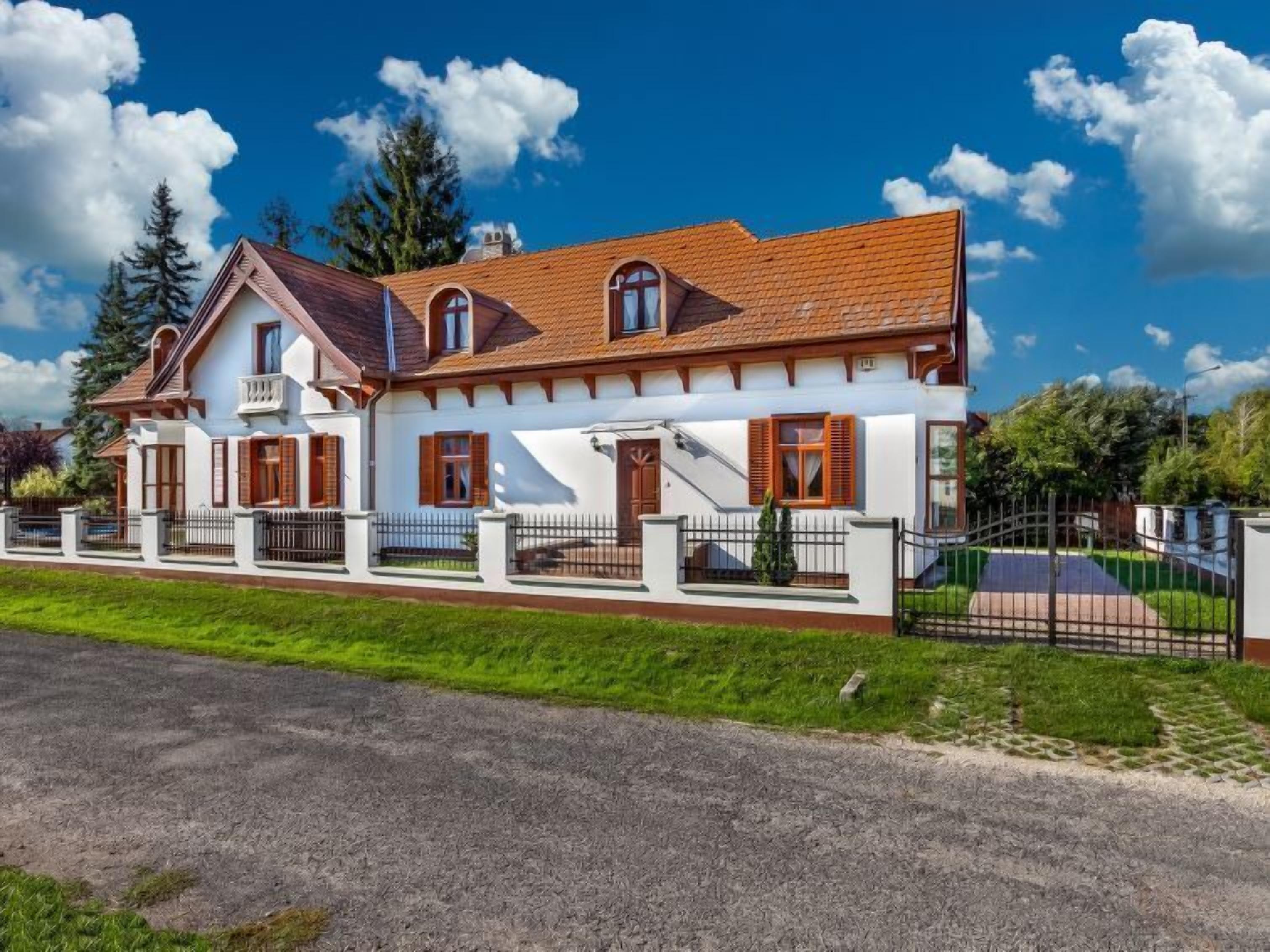 A two-story house with a red-tiled roof, white walls, and wooden shutters.