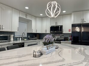 Una cocina moderna con armarios blancos, una isla central, un refrigerador de acero inoxidable y una lámpara colgante original.