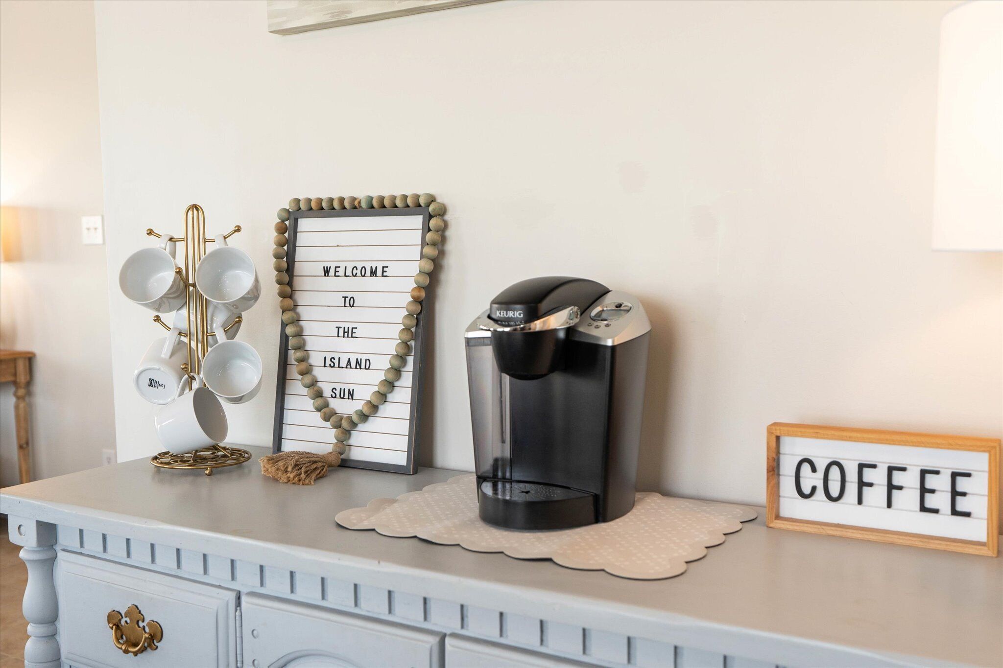 A coffee station with a coffee maker, a sign that says "WELCOME TO THE ISLAND SUN," and a sign that says "COFFEE."