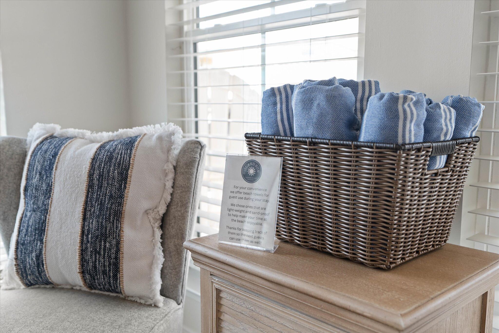 Un panier en osier rempli de serviettes bleues est posé sur une table, à côté d’une chaise sur laquelle se trouve un coussin à rayures.