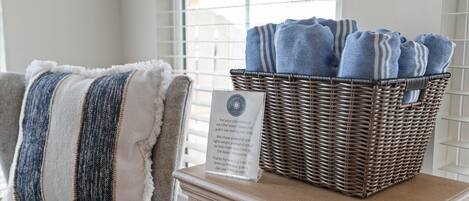 Un panier en osier rempli de serviettes bleues est posé sur une table, à côté d’une chaise sur laquelle se trouve un coussin à rayures.