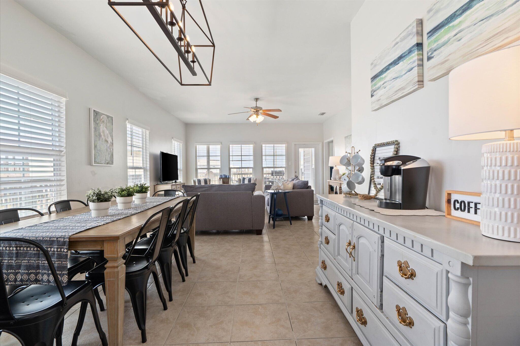 A modern kitchen with a dining area, featuring a long table, chairs, a sofa, and a coffee station.