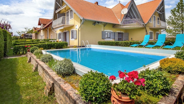 Un bâtiment à deux étages doté d’une piscine, de chaises longues bleues et d’un jardin bien entretenu.