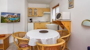 Une cuisine compacte avec des meubles en bois, un four à micro-ondes encastré et un coin repas avec des chaises en osier et une table ronde.