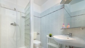 Une salle de bain moderne avec une douche à parois de verre, des toilettes blanches et un lavabo blanc avec un miroir au-dessus.