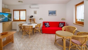 Un espace de vie compact comprenant un coin cuisine, un coin repas avec des meubles en osier, un canapé rouge et un téléviseur.