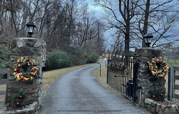 A stone gate with a Christmas wreath, leading to a paved path through a wooded area.