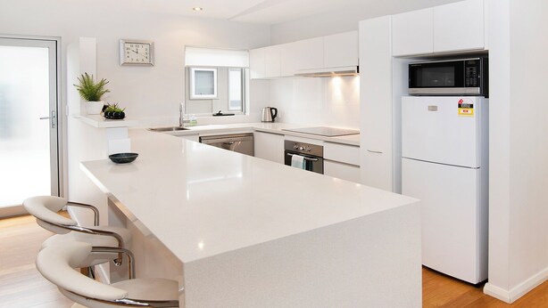 Una cocina moderna con una isla central, armarios blancos, microondas y refrigerador.