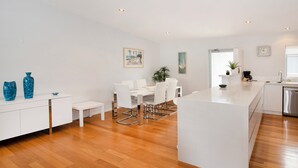 Una cocina moderna con armarios blancos, piso de madera y un comedor con sillas blancas y una mesa.