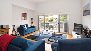 Una sala de estar moderna con un sofá azul, un televisor y un comedor con una mesa y sillas.