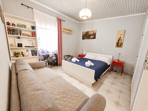 A modern bedroom with a bed, a sofa, a bookshelf, and a cityscape view.