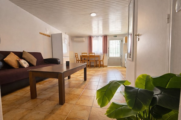 A room with a sofa, a wooden table, a dining table with chairs, and a large green plant.