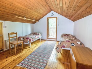 Une petite pièce agréable et chaleureuse, avec deux lits simples, une chaise en bois, un banc et un tapis à rayures.