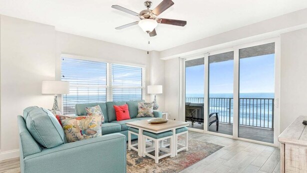 A spacious living room with a teal sofa, a coffee table, and a view of the ocean through large sliding glass doors. - High Tide Haven at the Aruba (Daytona Beach)