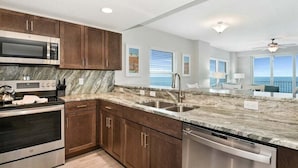 A modern kitchen with dark wood cabinets, stainless steel appliances, and a marble countertop. - High Tide Haven at the Aruba (Daytona Beach)