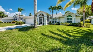 A residential house with a well-maintained lawn, palm trees, and a clear blue sky.