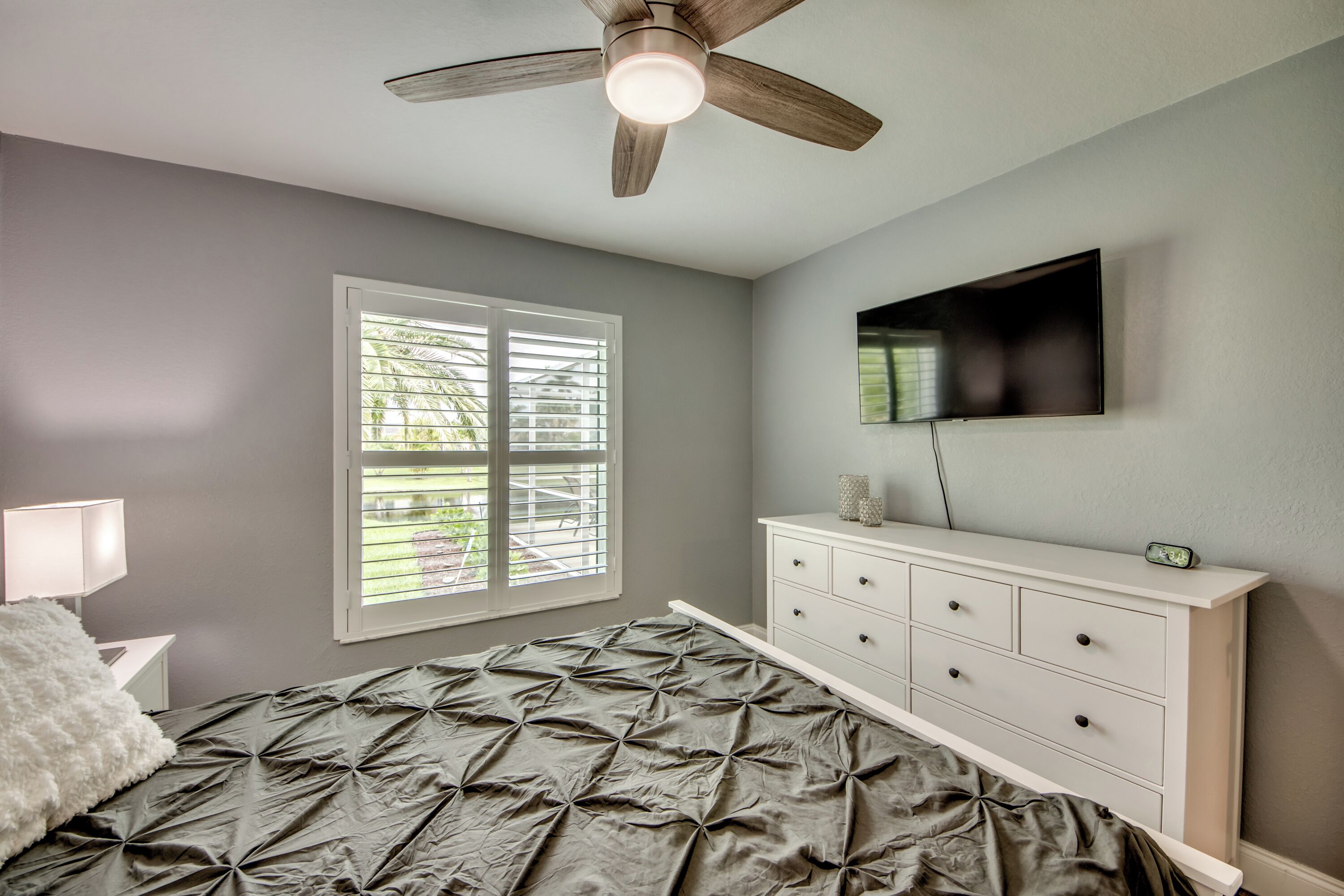 A bedroom with a bed, a dresser, a TV, and a ceiling fan.