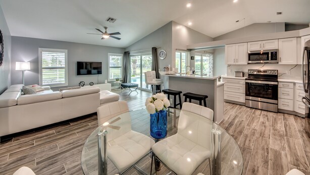 A modern living room with a glass dining table, white sofa, and a blue vase.