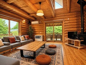 A log cabin interior with a sofa, table, ottomans, TV, fireplace, and large windows. - Rental Villa No 818 LDK 18 tatami mats  Western / Yama-gun Fukushima (Yama-gun)