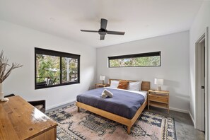 A bedroom with a bed, bedside tables, a ceiling fan, and large windows.