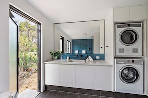 Un baño moderno con un espejo grande, un lavamanos, una lavadora y vistas al exterior con zonas verdes.