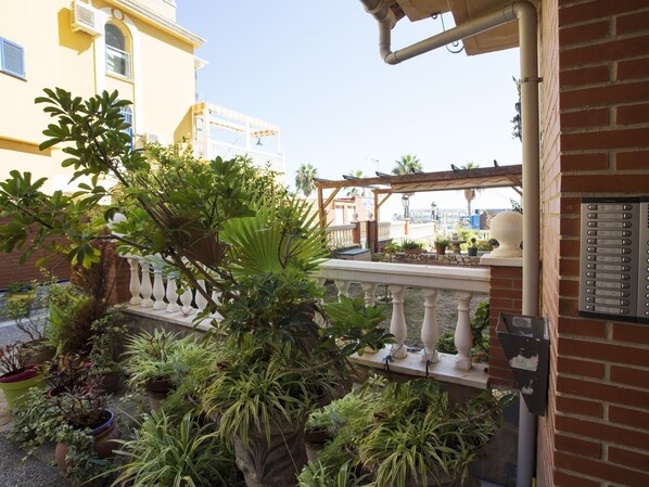 Ein Balkon mit Topfpflanzen, einem weißen Geländer und einem Gebäude mit gelben Wänden im Hintergrund.