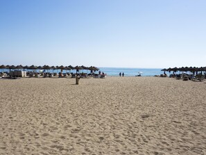 Ein Strand mit Liegestuhlreihen und Strandkörben, ein klarer Himmel und das Meer im Hintergrund.