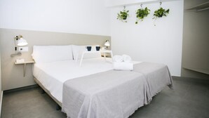 Une chambre d’hôtel moderne avec un grand lit, des tables de chevet, une plante suspendue et un luminaire au plafond.