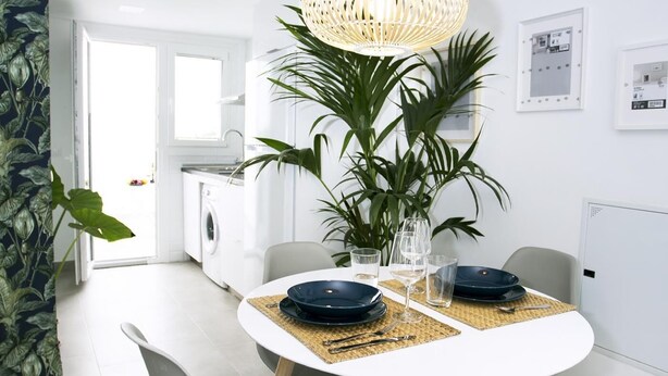 Un espace repas moderne avec une table blanche, des chaises grises et une plante au centre.