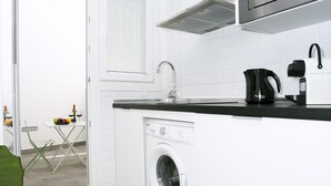 Une cuisine compacte équipée d’un lave-linge, d’une machine à café et d’une fenêtre avec des stores.