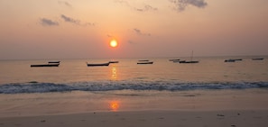 A beach with boats and the sun setting in the background.
